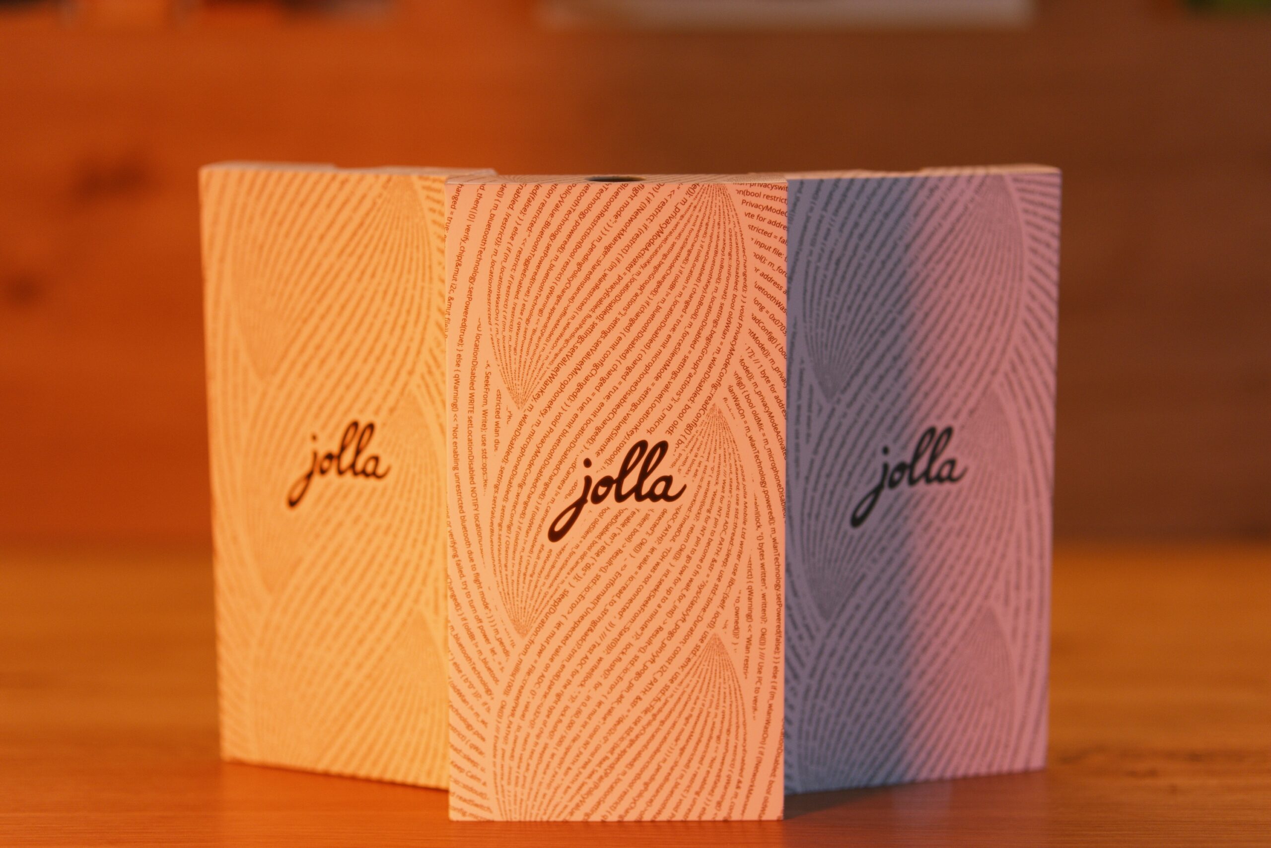 Die Verpackung der Jolla Phone, Glas und The Other Half nebeneinander. Alle Karton im selben Design. In der Mitte steht groß jolla umringt von einer Buchstabenspirale (Programmiercode) 