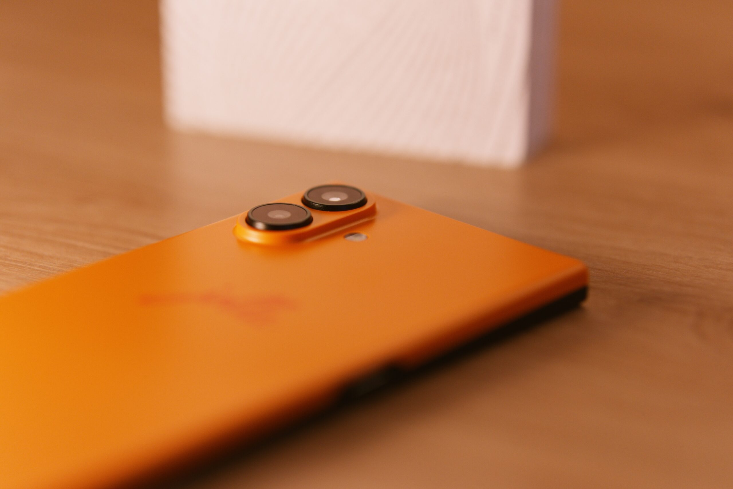 Das jolla Phone liegt am Bauch. Die Rückseite (Orange). Links oben die Kamerabuckel + LED, mittig unscharf jolla Schriftzug. 