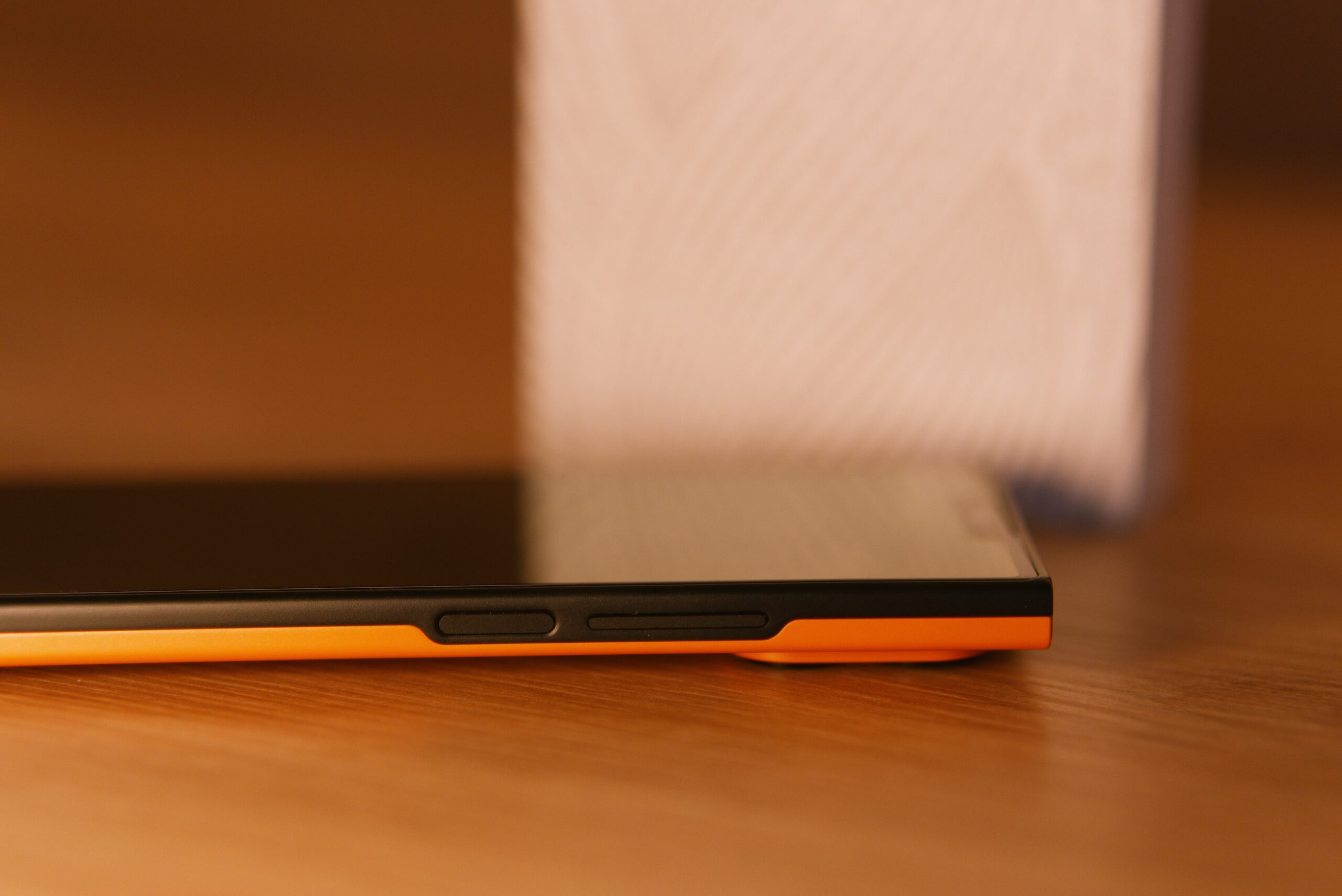 Das jolla Phone liegt am Rücken mit ausgeschalteten Display von Seitlicher Ansicht (Rechts). Man sieht links den Powerbutton (mit Finterpringt) und rechts Lautstärke Tasten.