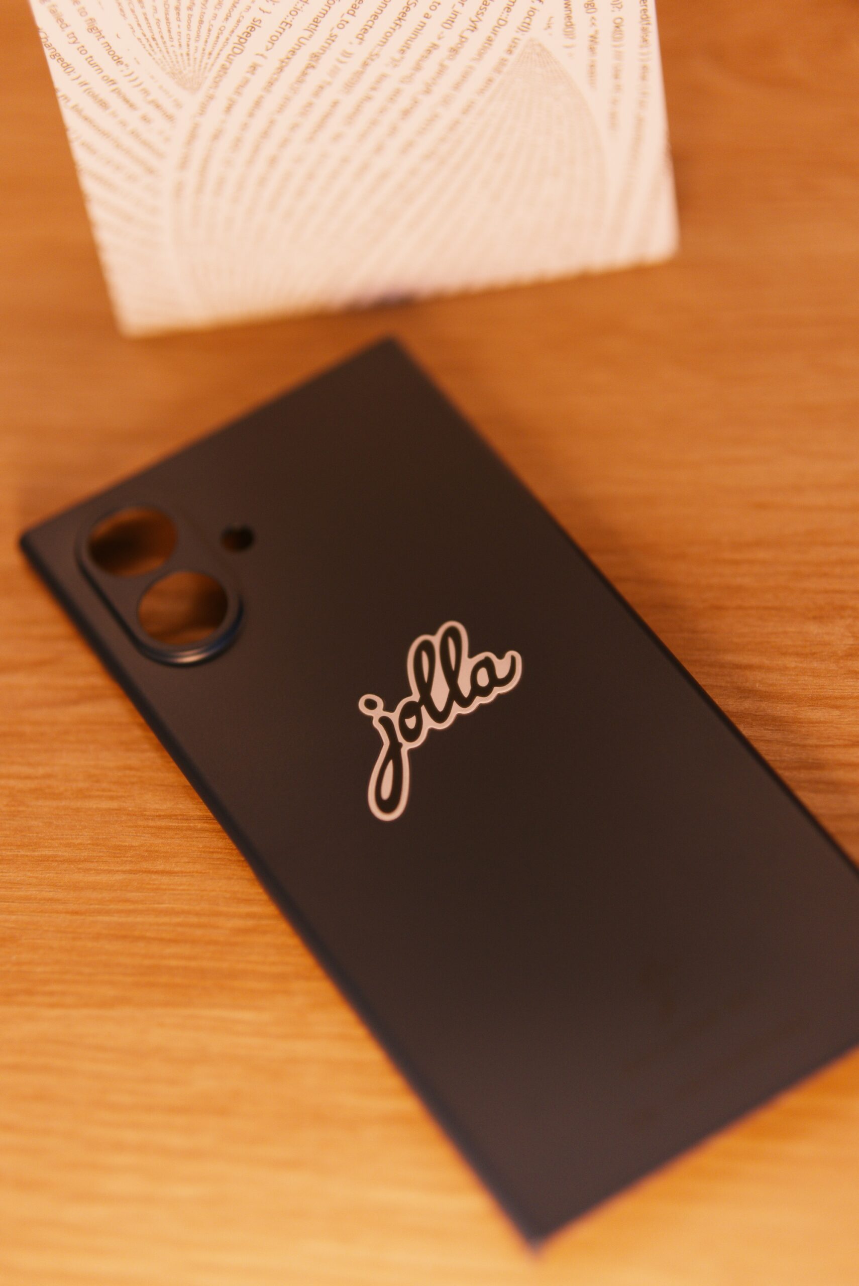The Other Half in Inari Blue. Mittig das jolla Logo am Cover.  Im Hintergrund die weiße Verpackung mit jolla Schriftzug umschlungen von einer Buchstabenspirale (Programmiercode)